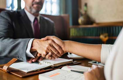 man in suit shaking hands with person at table with documents